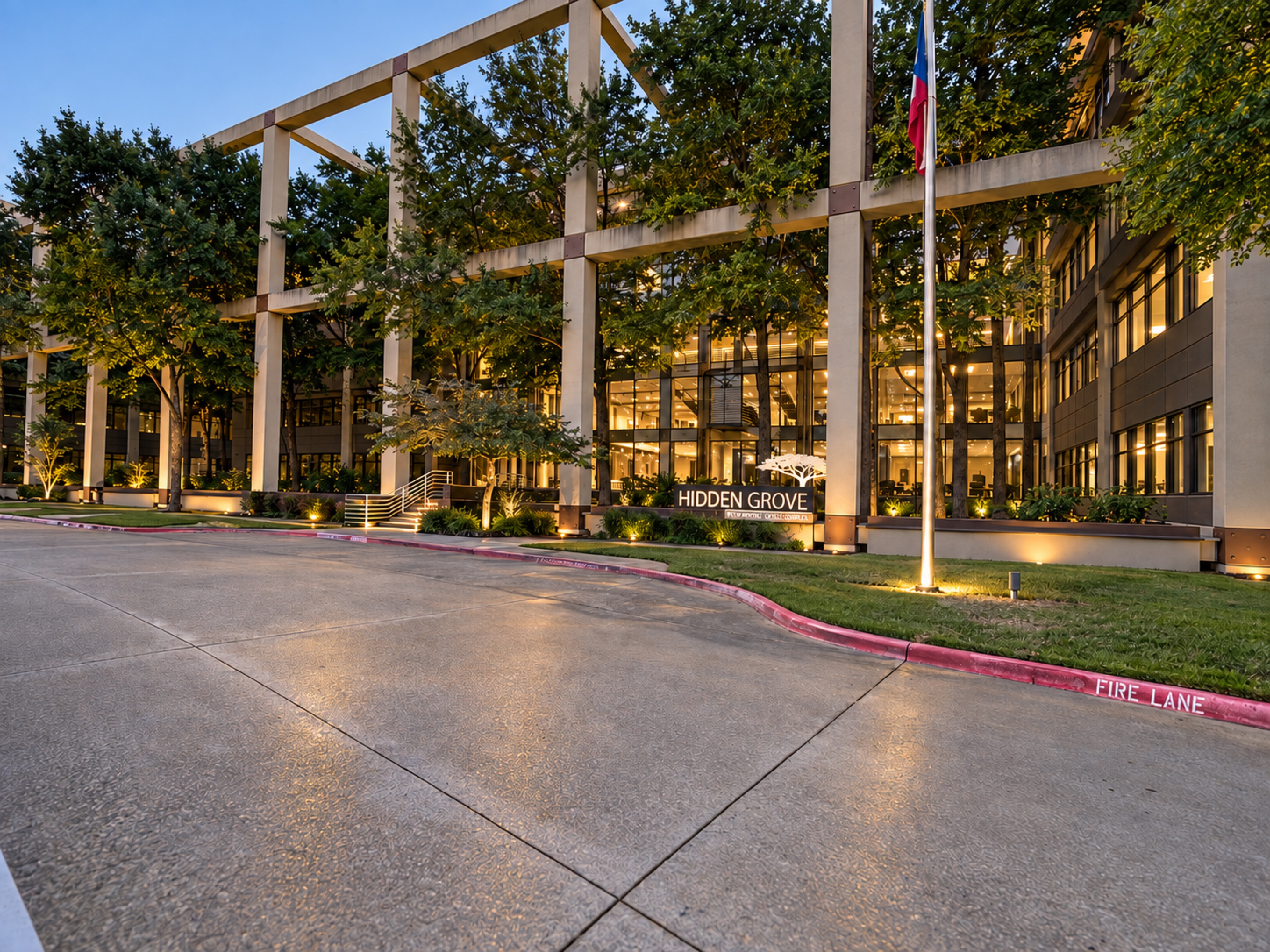 Hidden Grove building at dusk, framed by trees and a Texas flag